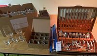 Wide photo of stemware, shot glasses, and Holmes & Edwards vintage silverplate flatware set in case with additional sterling flatware pieces.