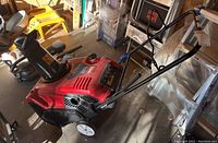 Side view of snow blower showing red housing, chute and wheels