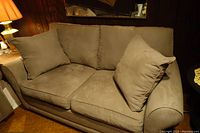 Light gray microfiber loveseat with loose seat and back cushions shown with two matching pillows in a cozy room setting.