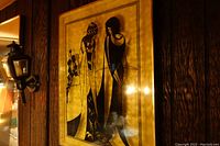 Photo of framed painting on wood wall showing two black silhouetted female figures with patterned details against gold background.