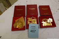 Lot of three Camerlane 24K gold finish Christmas ornaments displayed with their original red boxes on a white fabric background.