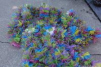 Photo showing multiple large decorative Easter garlands featuring bright blue, yellow, purple, and pink foliage and buds laid out on concrete ground.