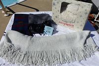 Lot displayed on table outdoors, showing white scarf with fringe, two patterned scarves, and boxed white slippers.