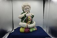 Front view of the ceramic Mrs. Santa Claus figurine knitting with colorful yarn balls in green dress and glasses.