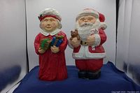 Front view of the two hand-painted wooden figurines of Santa and Mrs. Claus on a blue cloth background.