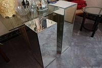 Two mirrored rectangular boxes placed on a carpeted floor beside a glass table with other home decor items visible.