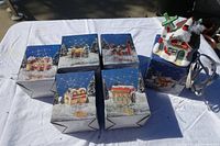 Six boxed 1994 lighted Santa village buildings arranged on white tarp outdoors, one building outside box showing colorful winter holiday design with Santa figure.