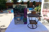 Photo of the brown metal tabletop lantern positioned next to its original Garden Candlelight product box on an outdoor table.
