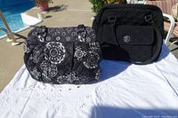 Two quilted bags displayed on white cloth by poolside, one solid black with front flap pocket, the other black with white medallion pattern.