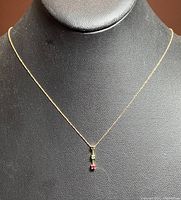 Full view of the gold necklace with pendant displayed on a black stand.