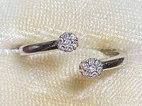 Top-down view showing the open ring design with two diamond clusters at each end on a fabric background.