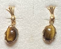 Front view of a pair of earrings with oval Tiger's Eye stones in gold setting.