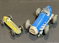 Blue Schuco Micro Racer #1042 race car alongside yellow Maserati 4CL T/1948 race car, showing size comparison and wheel details.