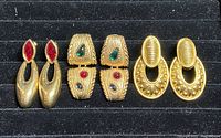 Photo showing four pairs of Swarovski gold-toned costume earrings with various crystal colors and designs laid out on black background.