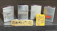 Four vintage lighters and one pack of Ronson flints displayed in a row