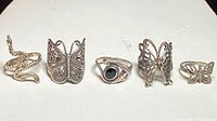 Top view of all five rings in a row showing different designs including snake shape, butterfly motifs, and black stone ring.