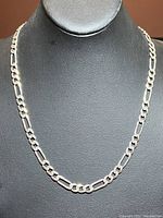Front view of the silver chainlink necklace displayed on a black stand, showing the alternating link design and polished silver finish.