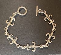 Full view of silver fleur de lis bracelet laid flat to show design, length, and clasp style.