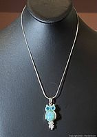 Front view of the sterling silver owl pendant necklace with bright blue stones on the eyes and a light blue Lorimar stone as the body.