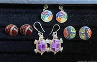Four pairs of vintage enamel earrings on display, featuring multiple colorful designs and shapes, one pair with dangle style