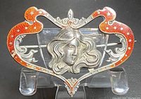 Front view of an antique sterling silver brooch with repousse detail, red enamel, and female face motif in the center.