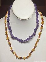 Two beaded necklaces displayed on white bust, amber and amethyst nuggets distinctly visible