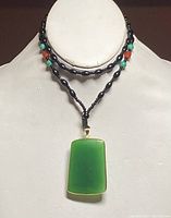 Front view of beaded necklace displayed on bust with jade pendant.