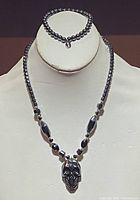 Frontal view of the hematite necklace displayed on a stand showing the detailed skull pendant and the beaded chain
