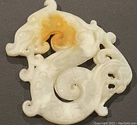 Close-up front view of the white jade dragon carved pendant with brownish-orange patina.