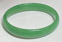 Green jade bangle bracelet on neutral background showing smooth polished surface and round shape.