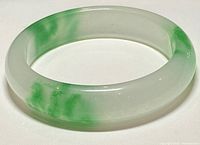 Side view of the jade bangle bracelet showing translucent white and green hues with glossy polished finish.