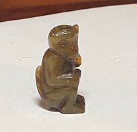 Front-angle view of the miniature carved jade monkey pendant on a flat surface, showing the details of the monkey's face and body posture.