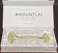 Jade facial roller in original satin-lined box with slogan and branding visible inside lid.