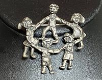 Front view of the silver pendant showing five children holding hands in a circle with distinctive details and a smooth finish.