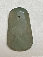 Front view of the jade pendant showing smooth polished surface, green color with natural flaws, and a drilled hole near the rounded top.
