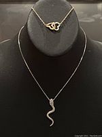 Front display image showing both necklace and bracelet on a black stand, highlighting the snake pendant and heart charms.