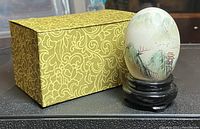 Photo showing the hand painted egg on its black wooden stand next to the original patterned box