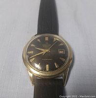 Front view of the vintage Certina automatic wristwatch showing the black dial, gold-tone markers, hands, and calendar window.