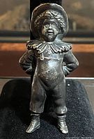 Front view of the vintage miniature solid cast metal boy figurine showing detailed facial features, ruffled collar, buttoned romper suit, and boots.