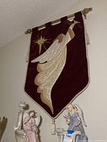 Full view of the angel quilted wall hanging hanging high on the wall with gold rods and finials.