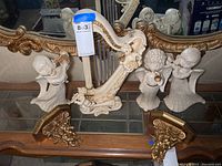 Three ceramic angels playing violin, trumpet, and flute, positioned behind two gilded angel corner shelves on a glass shelf.