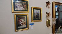 Three framed pictures with gold-colored frames mounted on a wall, showing various scenes including children in classic attire and a person on horseback.
