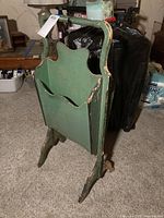 Full view of the antique wooden magazine holder painted green with wear visible on edges and legs.