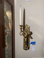 Front view of one brass candle sconce with a cherub figure holding a circular candle holder with a white taper candle.