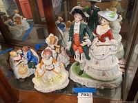 Five porcelain figurines on display with detailed 18th century costumes: standing couple and seated women, capturing full lot contents