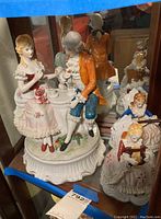Porcelain figurine of a boy and girl seated at a tea table, detailed clothing, pink rose, and ruffled dress
