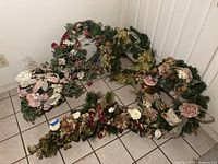 Overall view of five mixed faux floral wreaths with greenery and flowers, arranged on the floor.
