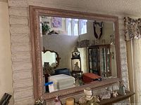 Full frontal view of the large framed beveled mirror reflecting a room with furniture and decorations.