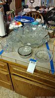 Photo of assorted clear glass punch bowls and relish trays arranged on a kitchen counter. Items include large and small bowls and divided serving trays with intricate cut glass patterns.