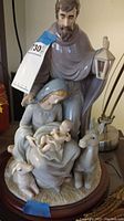 Full frontal view of Mary holding Baby Jesus, Joseph standing behind holding a lantern, sheep and donkey near base, statue on wooden base.